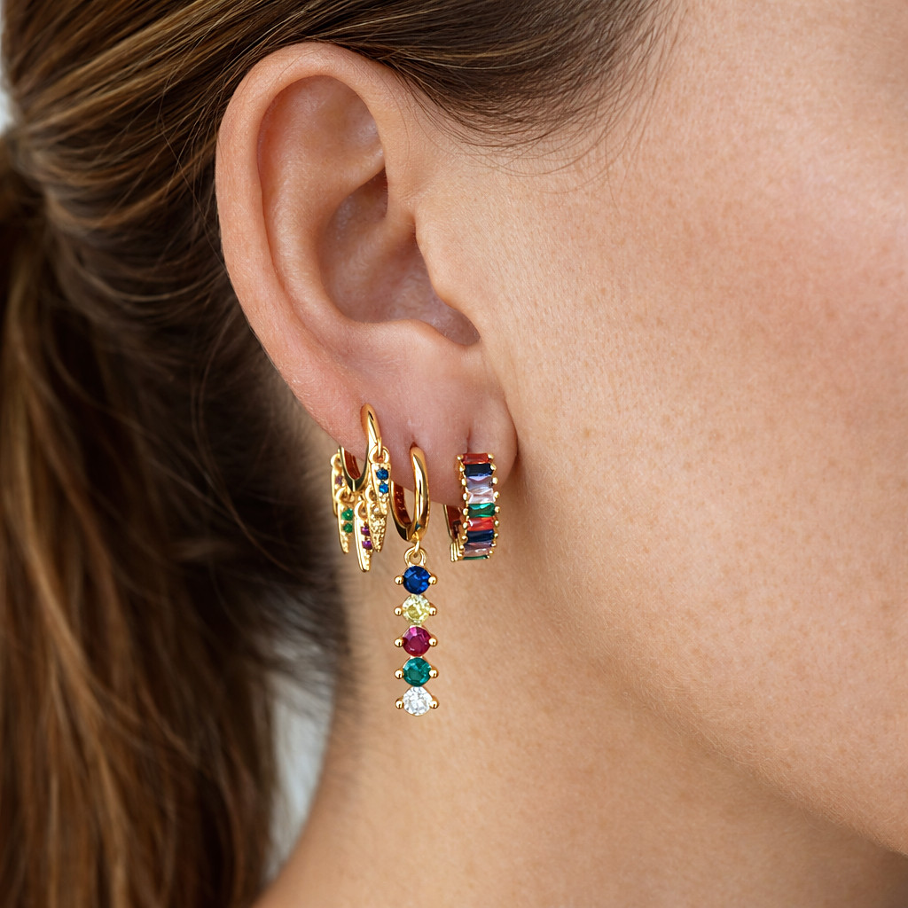 Combinación de aros pequeños dorados con circonitas y piedras de colores, puestos en la oreja