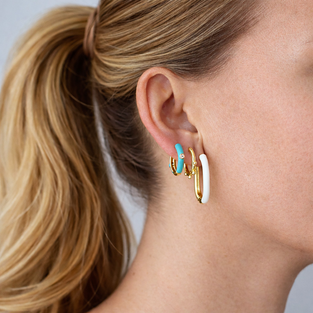 Combinación de aros pequeños dorados con esmalte turquesa y blanco, puestos en la oreja