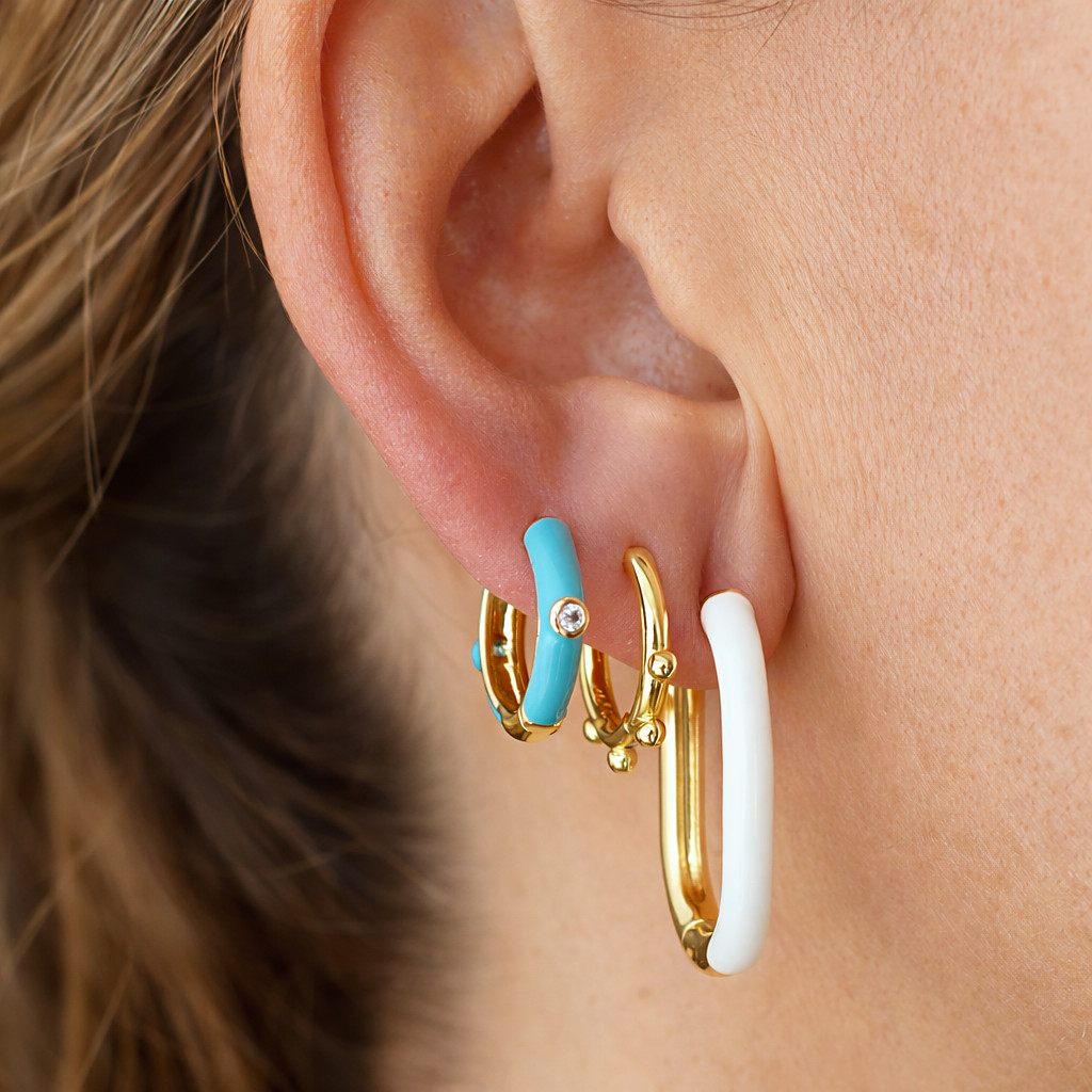 Aros dorados combinados en la oreja, uno con esmalte turquesa y otro con esmalte blanco