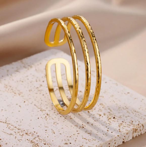 BRAZALETE FABIOLA. Brazalete rígido ajustable de acero inoxidable bañado en oro de 18k