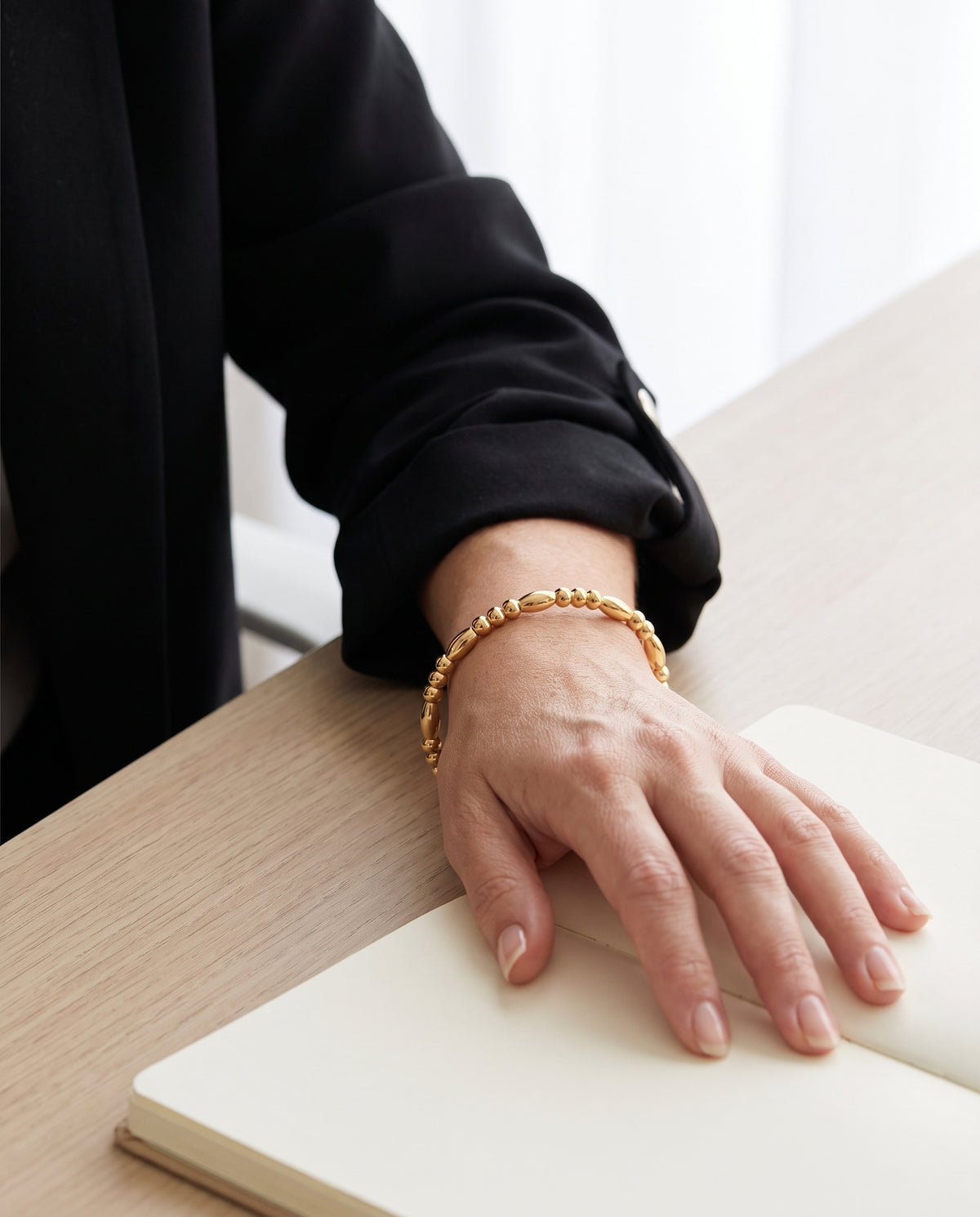 Brazalete Ágata rígido dorado con cuentas, puesto en la muñeca sobre una mesa de trabajo