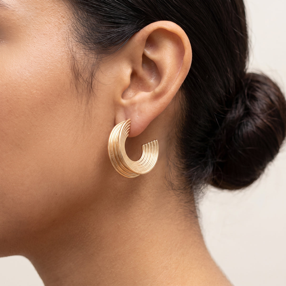 Pendientes Aura, aro en C con estrías bañado en oro, puesto en una oreja con el pelo recogido en un moño