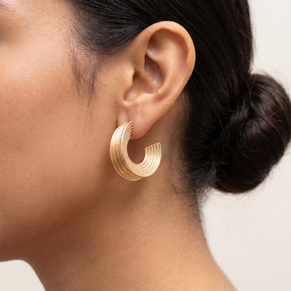 Pendientes Aura, aro en C con estrías bañado en oro, puesto en una oreja con el pelo recogido en un moño