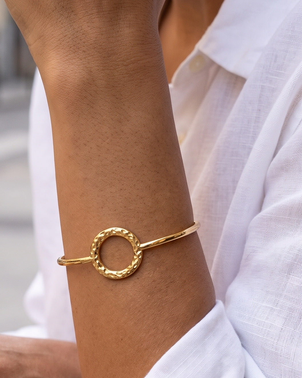 Brazalete Macarena dorado con círculo martillado, puesto en la muñeca de una mujer en una terraza