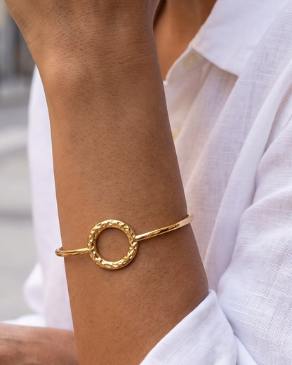 Brazalete Macarena dorado con círculo martillado, puesto en la muñeca de una mujer en una terraza