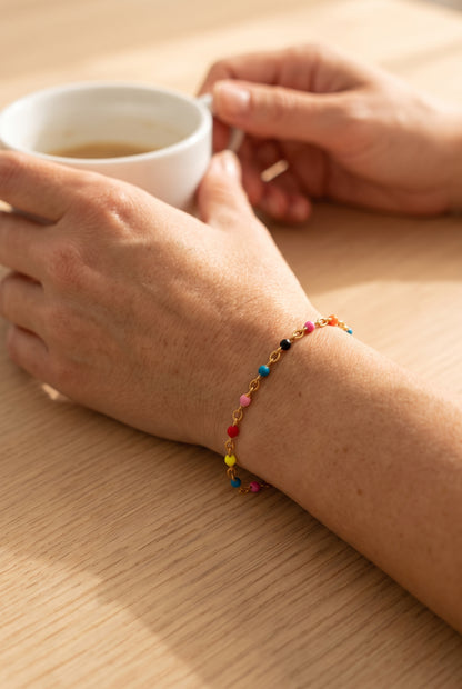 Muñeca con la Pulsera Maite, cadena dorada con cuentas de colores, sujetando una taza de café