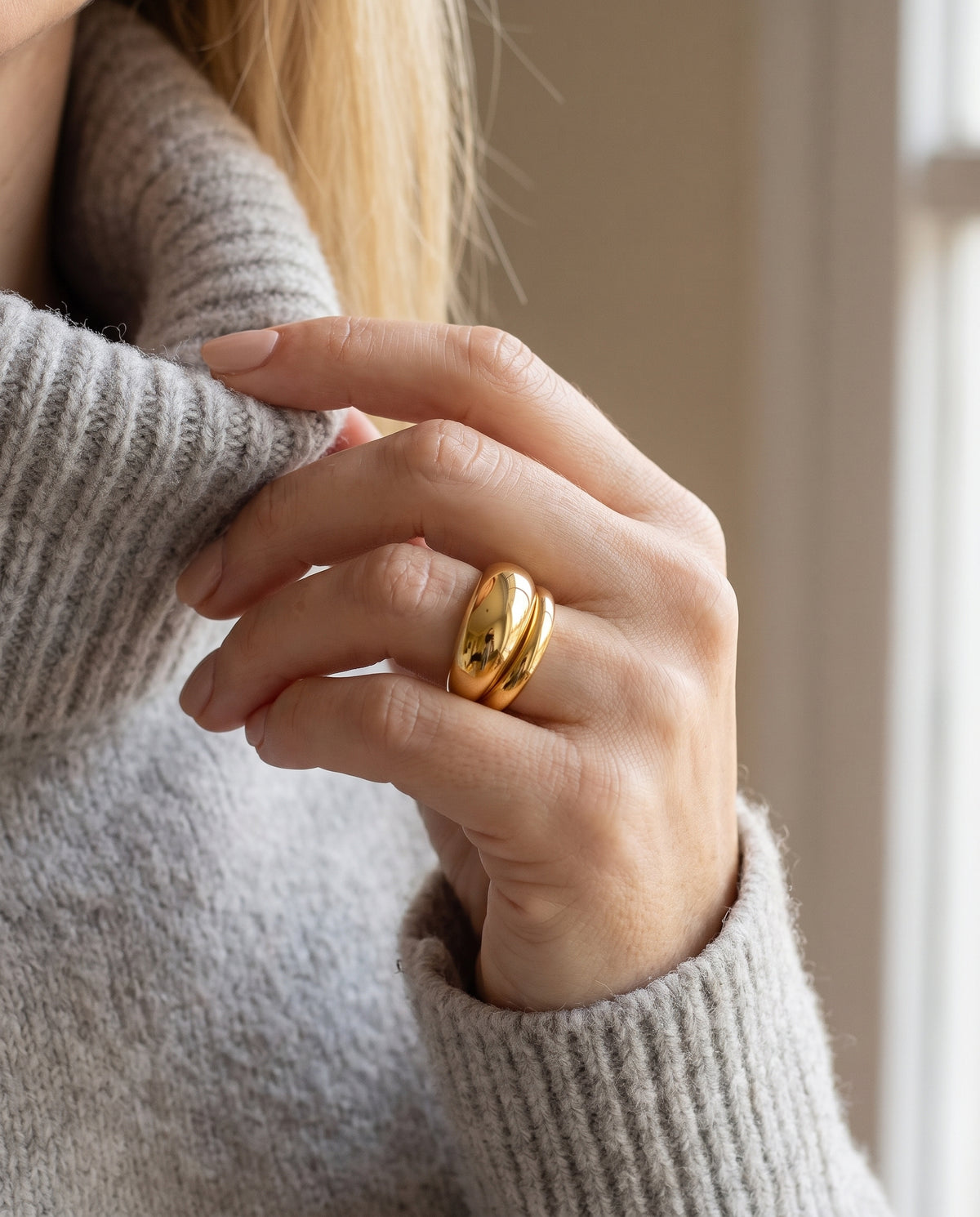 Anillo Ofelia ancho y abombado bañado en oro, puesto en la mano sobre un jersey gris