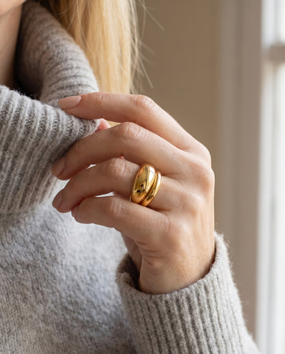 Anillo Ofelia ancho y abombado bañado en oro, puesto en la mano sobre un jersey gris