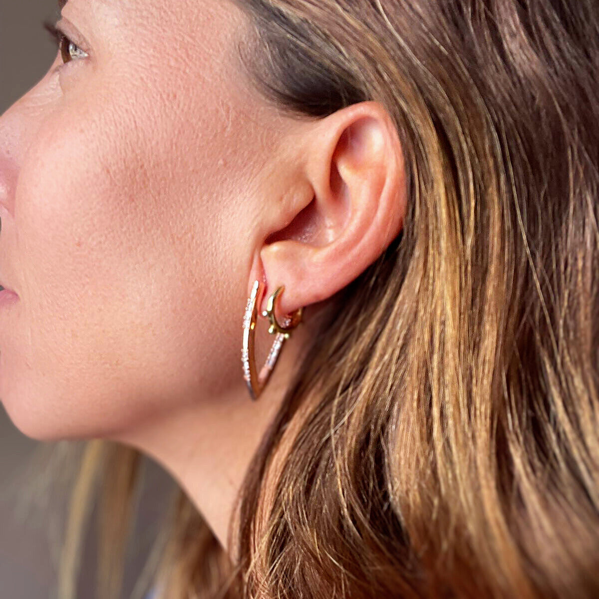 Pendientes de aro con forma de arpa en oro rosa, puestos en la oreja con otros aros