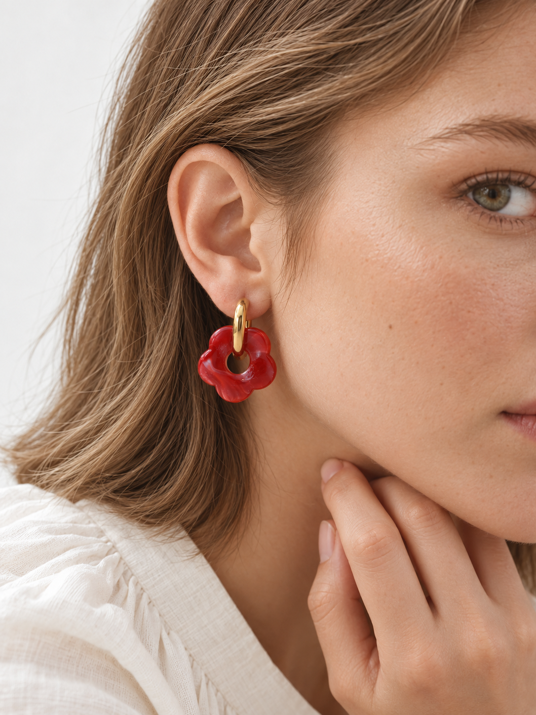 Pendiente de aro dorado con colgante de flor de acrílico rojo, puesto en la oreja