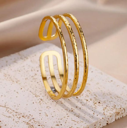 BRAZALETE FABIOLA. Brazalete rígido ajustable de acero inoxidable bañado en oro de 18k