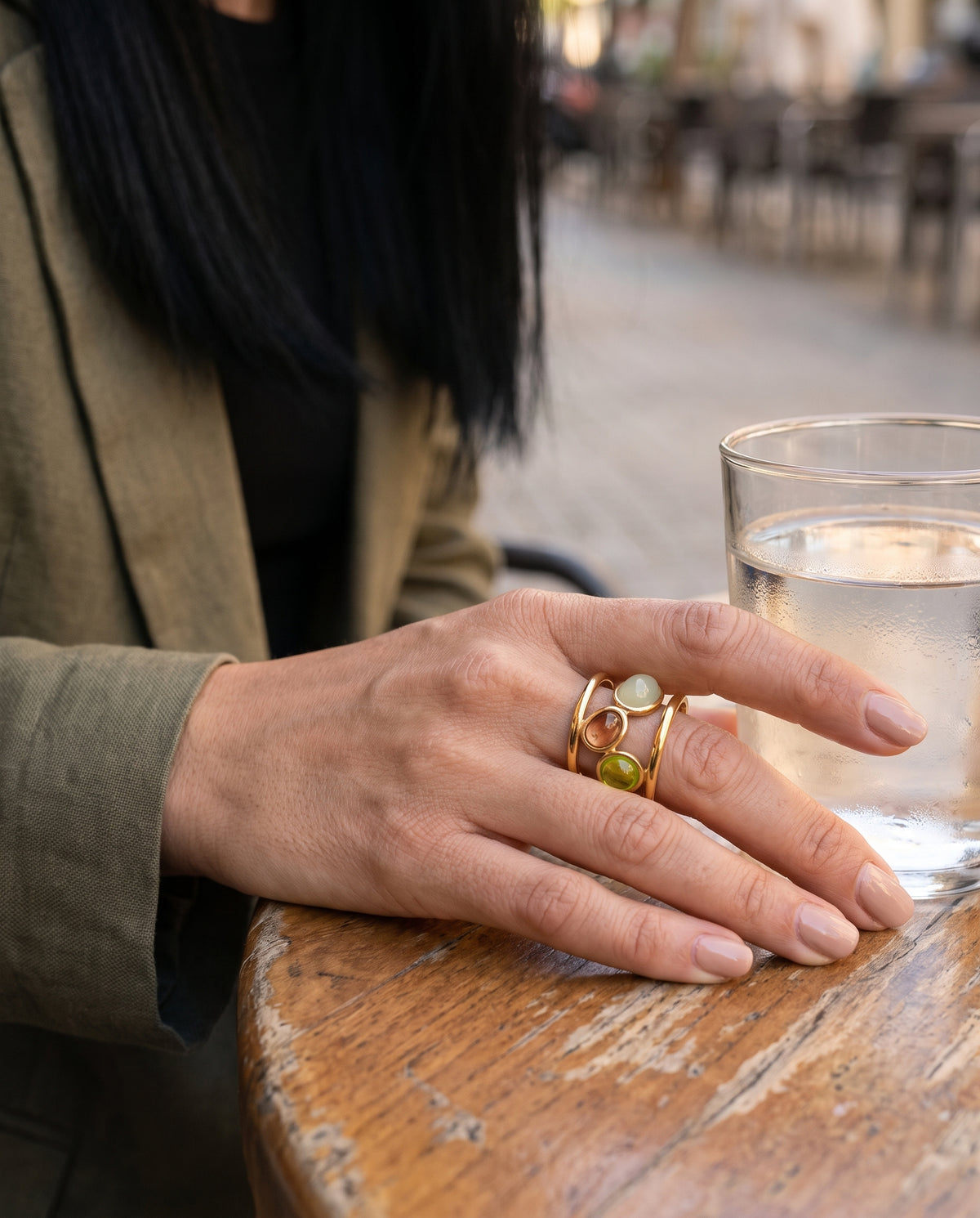 Anillo Sigrid dorado con tres piedras de colores, puesto en la mano en una terraza