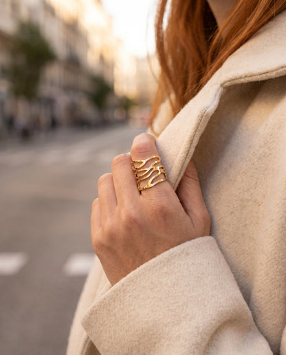 Anillo Talía de líneas onduladas bañado en oro, puesto en la mano sobre un abrigo crudo